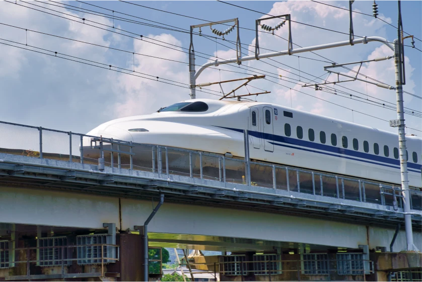 青い空と白い雲の下、雄大な自然を背景に、新幹線が鉄橋を渡る。